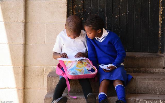 A young Zambian girl in a school uniform reading a book